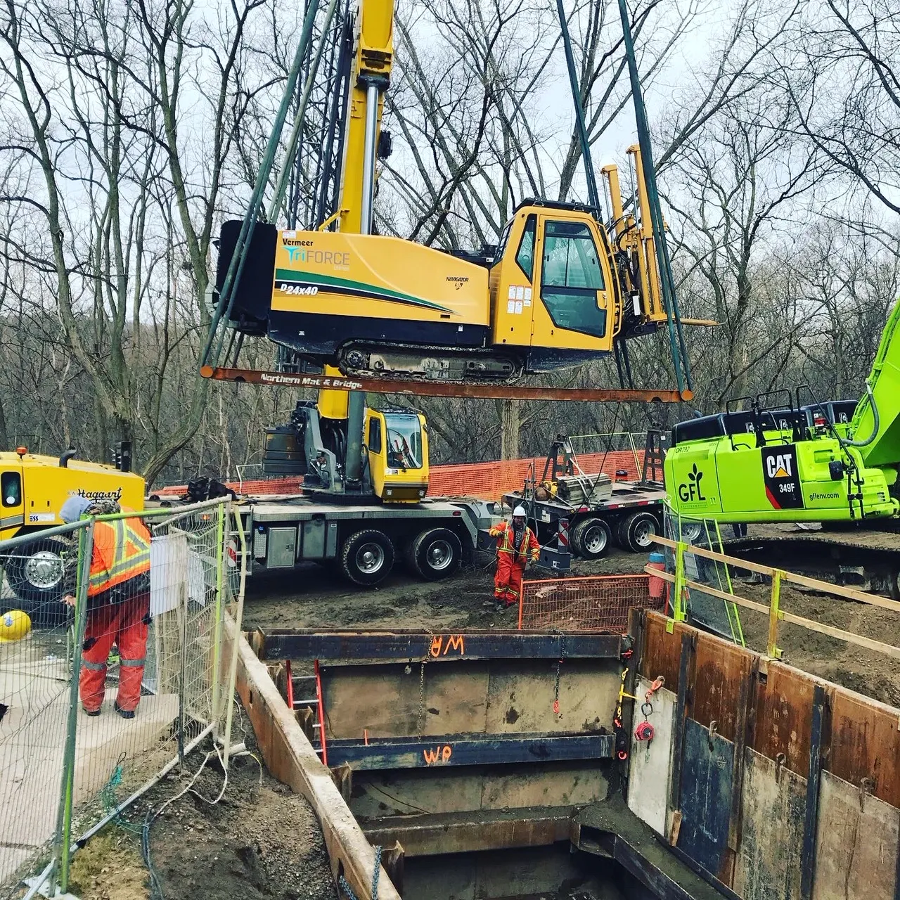 Crane lowering a directional drill rig into an excavation pit